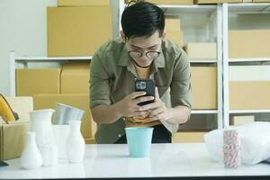 Young male online business owner using cellphone checking parcel box. photo