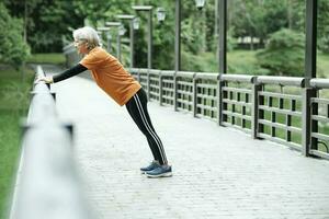 Athletic Senior woman stretching two arms in park. photo