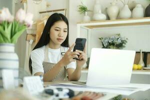 joven asiático mujer de negocios sentado en casa inspección producto y a contacto clientes. foto