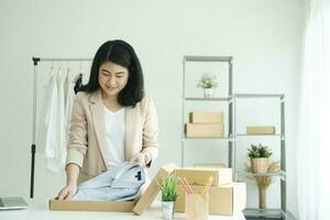 Asian female clothes shop owner folding a t-shirt and packing in a cardboard parcel box. photo