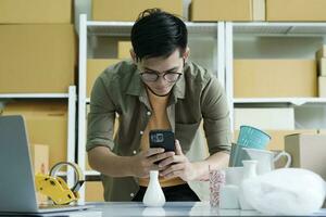 joven masculino en línea negocio propietario utilizando Teléfono móvil comprobación paquete o empaquetar caja. foto