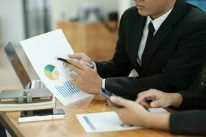 Businessmen working, discussing, analyzing using laptop and graphs. photo