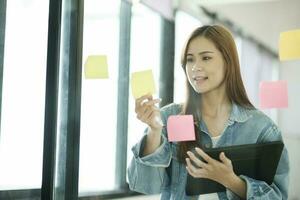 Young female student writing study plans on post-its on glass wall. photo