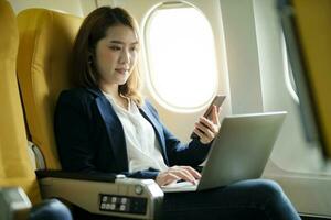 Business woman In a plane, works on using laptop computer and phone photo