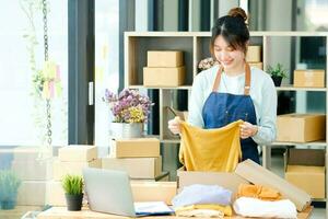 Asian female clothes shop owner folding a t-shirt and packing in a cardboard parcel box. photo