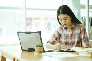 joven asiático mujer estudiar en frente de el ordenador portátil computadora y y utilizando auriculares a Fuera del sitio. foto