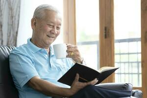 Relax elderly man sitting on sofa and reading interesting book in living room. photo