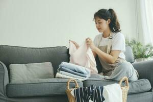 Young woman folding clothes on sofa at home. photo