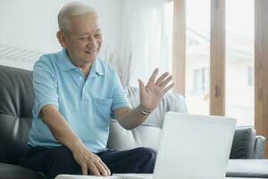 Elderly man making video call and waving at screen. photo