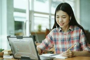 Young asian woman study in front of the laptop computer and and using headphones at offsite. photo