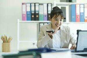 joven asiático mujer de negocios es trabajando a oficina utilizando móvil teléfono. foto