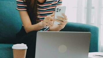 Happy Asian teen girl holding pad computer gadget using digital tablet technology sitting on the couch at home. Smiling young woman using apps, shopping online, reading news, browsing internet on sofa video