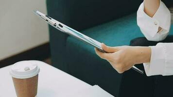 Happy Asian teen girl holding pad computer gadget using digital tablet technology sitting on the couch at home. Smiling young woman using apps, shopping online, reading news, browsing internet on sofa video