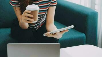 Happy Asian teen girl holding pad computer gadget using digital tablet technology sitting on the couch at home. Smiling young woman using apps, shopping online, reading news, browsing internet on sofa video