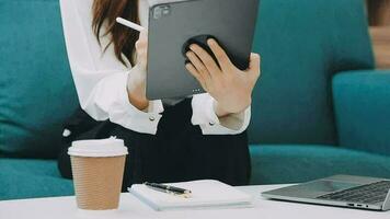 contento asiatico adolescente ragazza Tenere tampone computer aggeggio utilizzando digitale tavoletta tecnologia seduta su il divano a casa. sorridente giovane donna utilizzando app, shopping in linea, lettura notizia, navigazione Internet su divano video