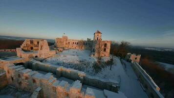 Aerial view of beautiful historic castle ruins on the hill in winter at sunset. Tenczyn Castle in Rudno, Poland. Filmed on FPV drone video