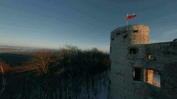 Aerial view of beautiful historic castle ruins on the hill in winter at sunset. Tenczyn Castle in Rudno, Poland. Filmed on FPV drone video