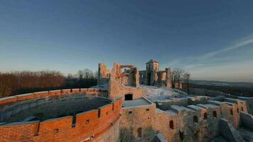 Aerial view of beautiful historic castle ruins on the hill in winter at sunset. Tenczyn Castle in Rudno, Poland. Filmed on FPV drone video