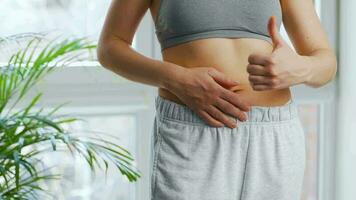 Woman puts on her pants, strokes her stomach and gives a thumbs up. Concept of healthy digestion and bowel function video