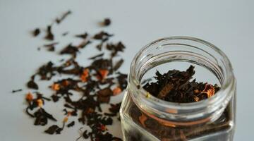 leaf tea with pieces of fruit in a jar, scattered tea, black tea, a jar of tea on a gray background, international tea day photo