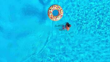 Aerial view of a man in red shorts swimming in the pool with an inflatable donut video