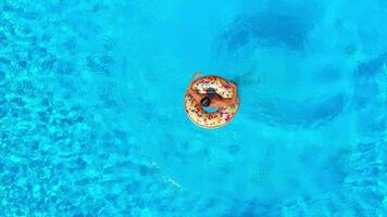 Aerial view of a man in red shorts swimming in the pool with an inflatable donut video