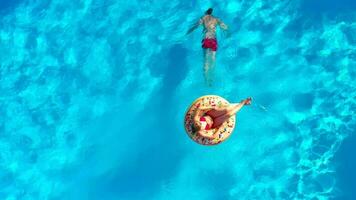 Couple having fun in the pool, the man dives and the woman lies on a donut video