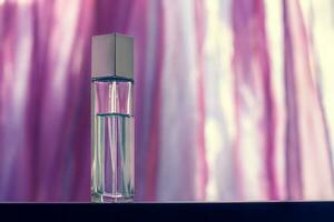 An elongated faceted perfume bottle stands on a blurry light pink background. Glass vial with a metal cap. Blank for mock up. Selective focus. Horizontal. photo