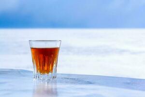 Chilled whiskey in a glass stands on ice against the background of blurry snow and sky. Orange alcoholic drink in a glass. Copy space. Side view. The background is blurry. Horizontal. photo