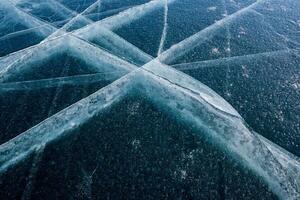 Very beautiful natural texture of the thick ice of Lake Baikal with long cracks in the form of a grid. Dark ice and light cracks. photo