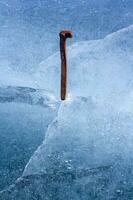 antiguo ferrocarril muleta martillado dentro el hielo de un lago. oxidado alfiler y azul derritiendo hielo con grietas y aire burbujas símbolo resistencia y firmeza. vertical. foto