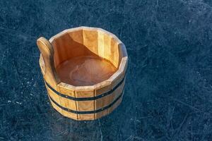 A wooden tub with ice inside is standing on the ice with cracks. Iron tightening rings connect parts of the tub. Sunny. Horizontal. photo