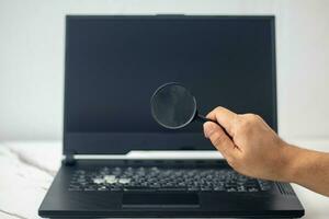 magnifying glass in hand looking at laptop to search internet photo