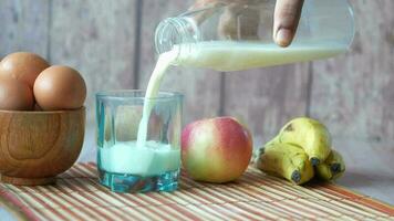 Pouring milk in a glass with banana, egg and apple on table video