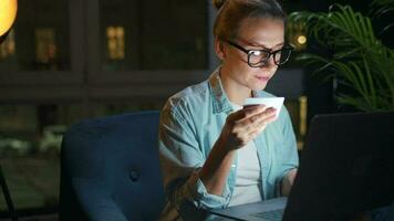 Woman is sitting in the armchair and makes an online purchase using a credit card and laptop at night video