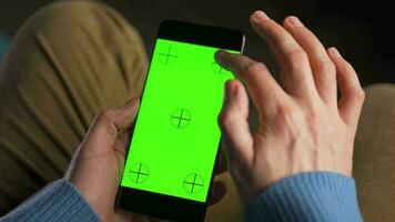 man använder sig av smartphone med grön mock-up skärm i vertikal läge och dricka kaffe. man bläddring internet, tittar på innehåll, videoklipp video