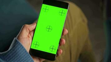 man använder sig av smartphone med grön mock-up skärm i vertikal läge och dricka kaffe. man bläddring internet, tittar på innehåll, videoklipp video