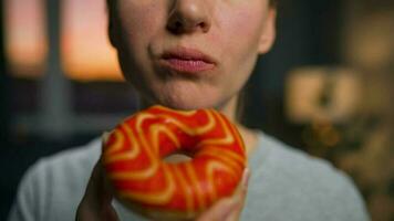 Sweet addiction concept. Woman eats orange donut closeup video