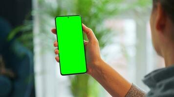 femme à Accueil en utilisant téléphone intelligent avec vert maquette écran dans verticale mode. fille navigation l'Internet, en train de regarder contenu video
