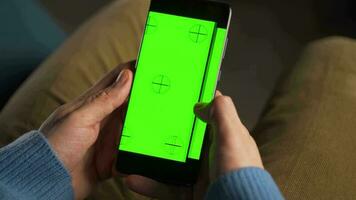 man använder sig av smartphone med grön mock-up skärm i vertikal läge och dricka kaffe. man bläddring internet, tittar på innehåll, videoklipp video