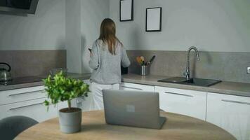 donna in piedi nel casa accogliente cucina uso il computer portatile fare libero professionista opera, chat con qualcuno, segreteria e-mail. concetto di a distanza opera video