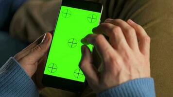 Mens gebruik makend van smartphone met groen mock-up scherm in verticaal mode en drinken koffie. Mens browsen internetten, aan het kijken inhoud, videos