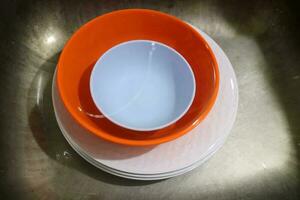 White and orange plates and bowls piled in the sink photo