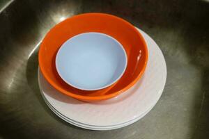 White and orange plates and bowls piled in the sink photo