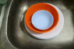 White and orange plates and bowls piled in the sink photo