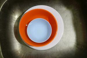 White and orange plates and bowls piled in the sink photo