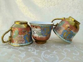 Several vintage cups with floral textures are uniquely arranged on the table photo