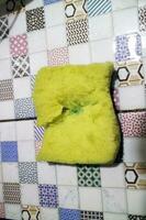 A broken yellow foam used for washing dishes is placed on the tile photo