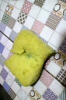 A broken yellow foam used for washing dishes is placed on the tile photo