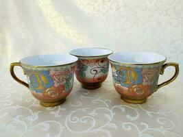 Several vintage cups with floral textures are uniquely arranged on the table photo